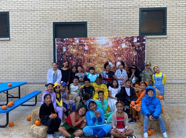 5th-grade students proudly display decorated pumpkins at a Halloween Pumpkin Festival, showcasing their creativity with colorful designs and festive autumn decorations.